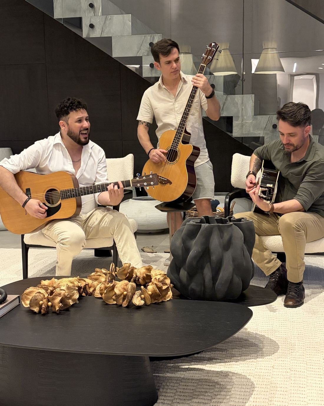 Três músicos da VELT tocando violão de perto em uma sala de estar