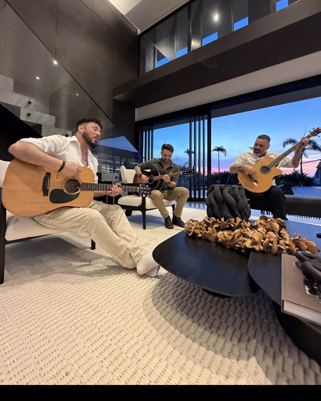 A VELT tocando em uma sala de pé-direito alto, com vidraças abertas para o céu da hora azul